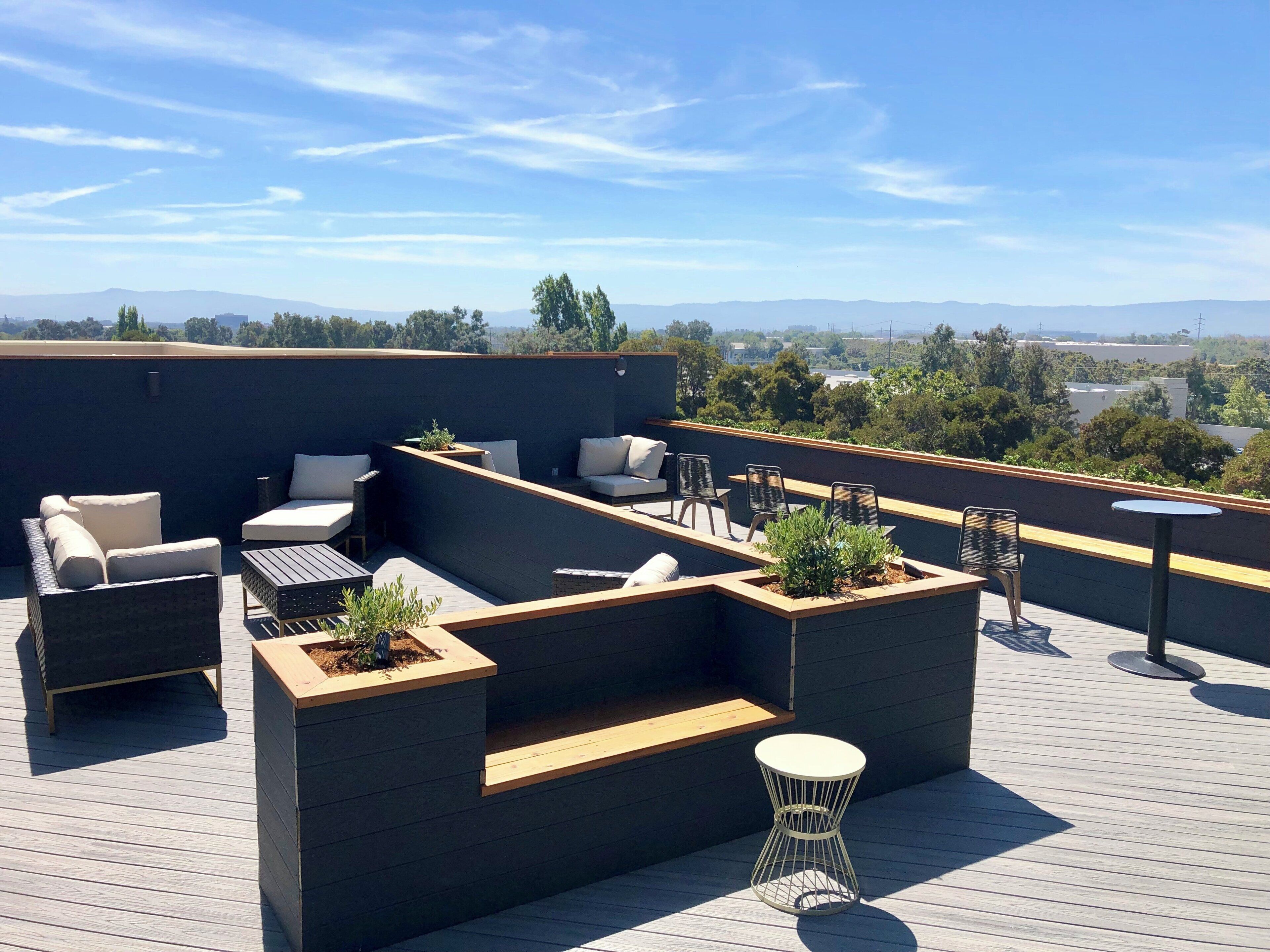 A rooftop terrace with outdoor seating, a small table, and planters.
