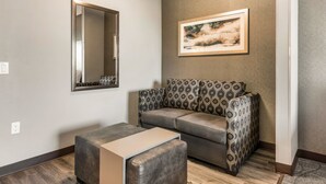 A living room with a gray sofa, a patterned ottoman, a mirror, and a framed picture on the wall. - Holiday Inn & Suites Silicon Valley - Milpitas by IHG (Milpitas)