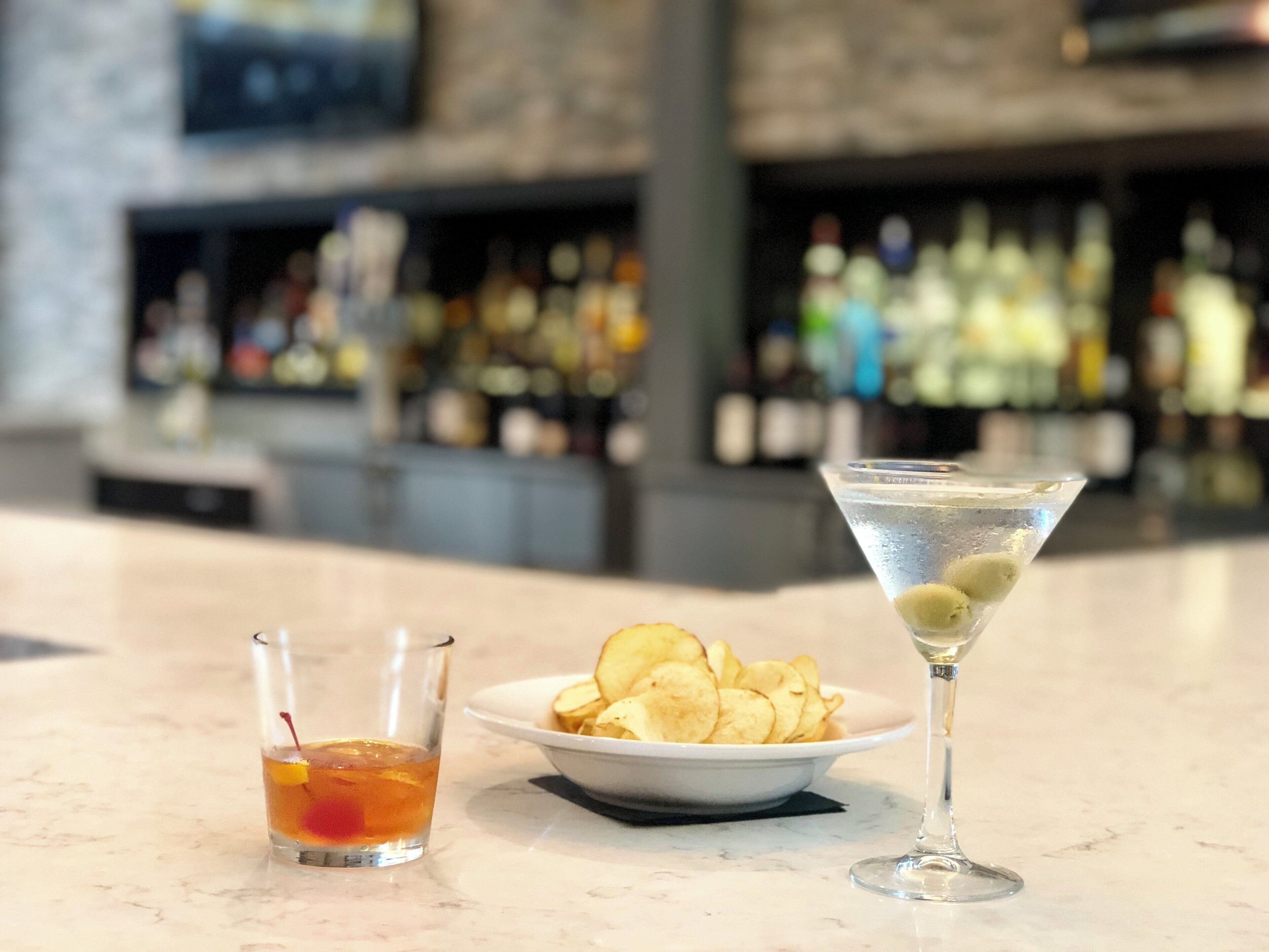 Un bar con una copa de martini y un vaso pequeño con una cereza en el borde.