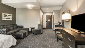 A hotel room with a sofa, a chair, a TV, a dresser, and a small table. - Holiday Inn & Suites Silicon Valley - Milpitas by IHG (Milpitas)