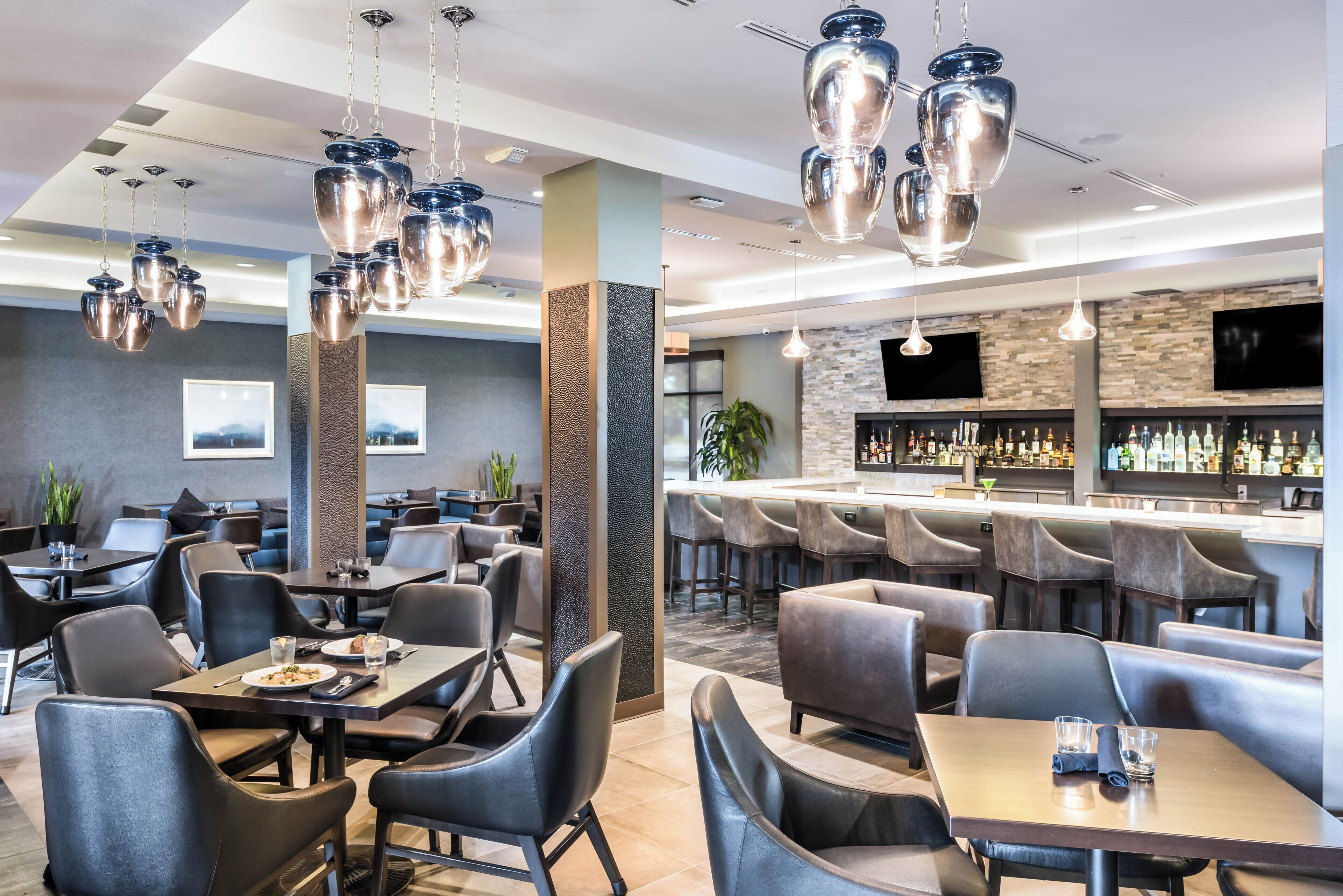 A modern restaurant with multiple seating areas, including tables and booths, and a bar with a variety of liquor bottles.