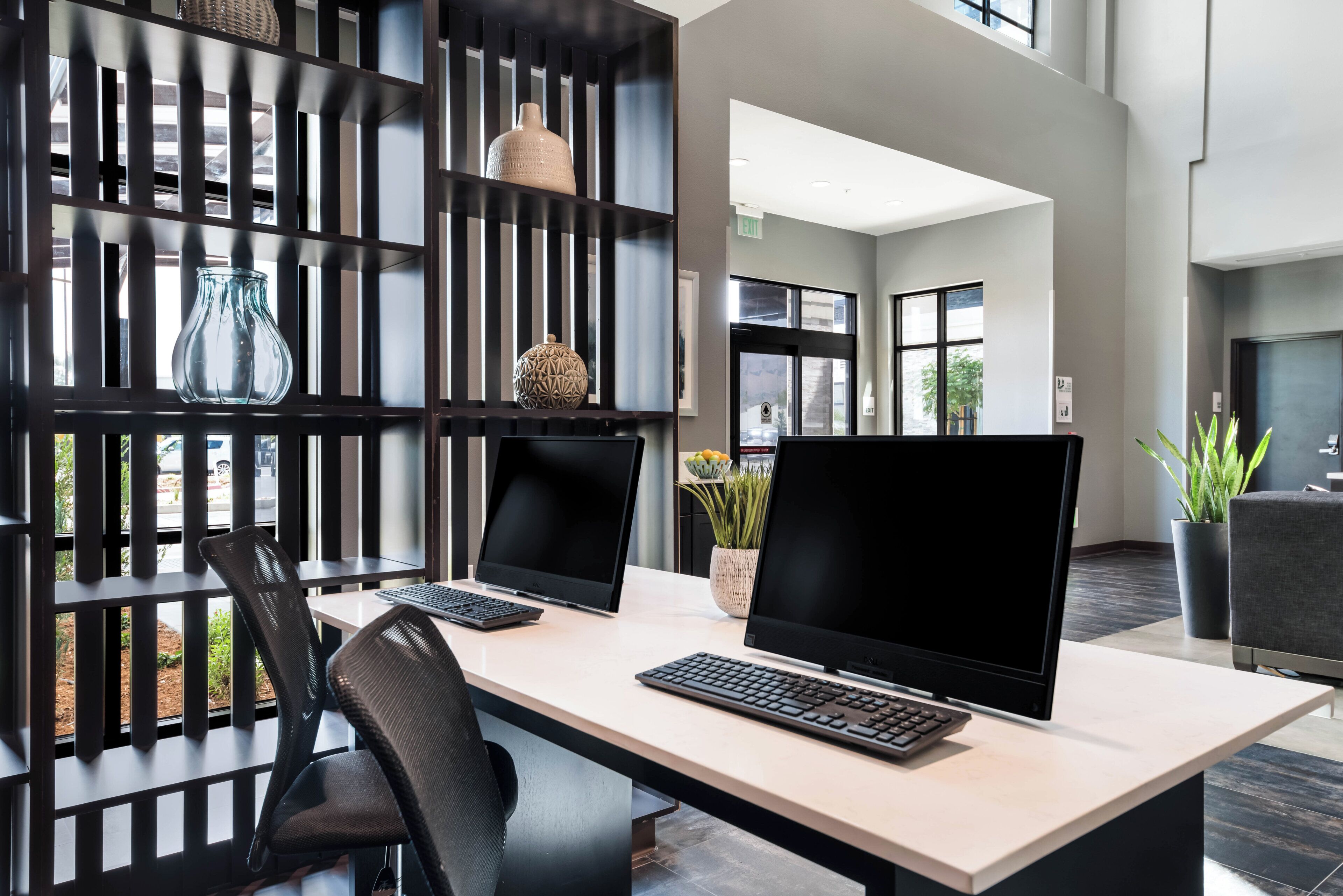 Un espacio de oficina moderno con dos escritorios, cada uno con un ordenador y teclado, una silla, y objetos decorativos en estanterías.