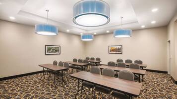 A conference room with tables and chairs, blue pendant lights, patterned carpet, and framed pictures on the walls.