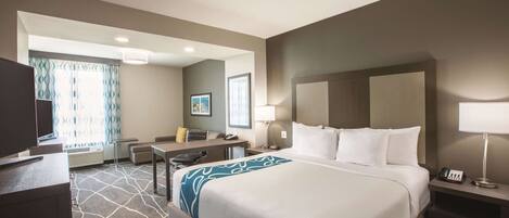 A hotel room with a large bed, a desk, a chair, a TV, and a window with curtains.