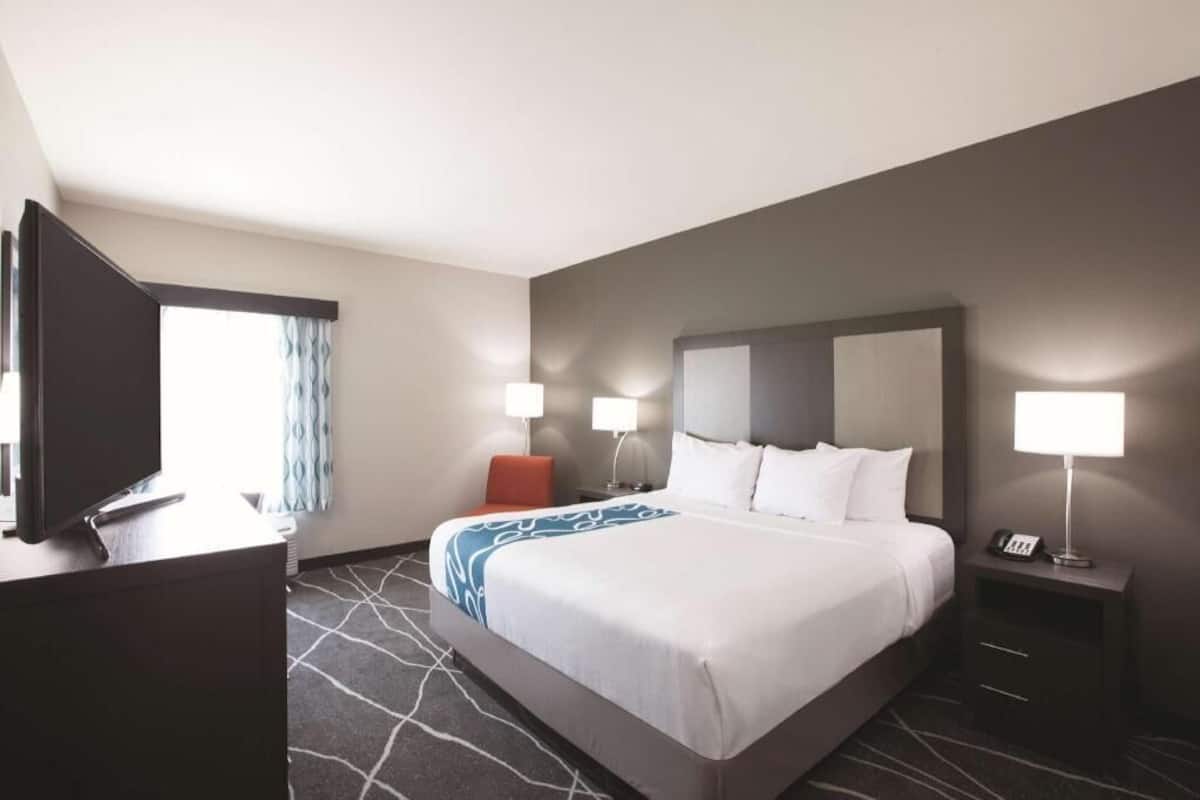 A hotel room with a bed, bedside lamps, a desk with a TV, and a window with curtains.