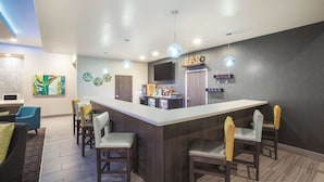 A modern kitchen with a bar area, featuring a large island with bar stools, a television above the bar, and a decorative wall with a 'BAR' sign. - La Quinta Inn & Suites by Wyndham Tulsa Broken Arrow (Broken Arrow)