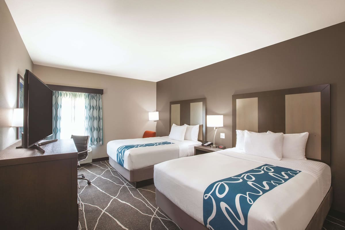 A hotel room with two beds, a desk, a chair, a TV, and a window with curtains.