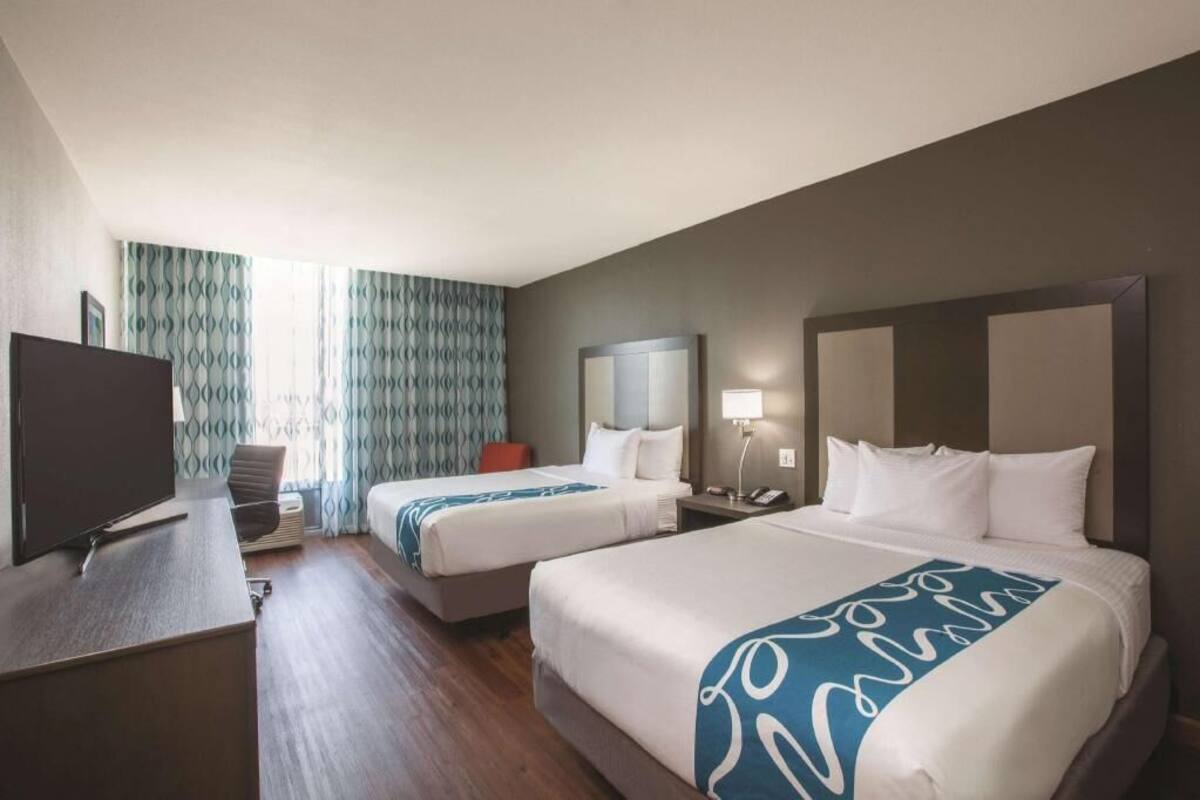 A hotel room with two beds, a desk with a TV, a chair, and a window with curtains.