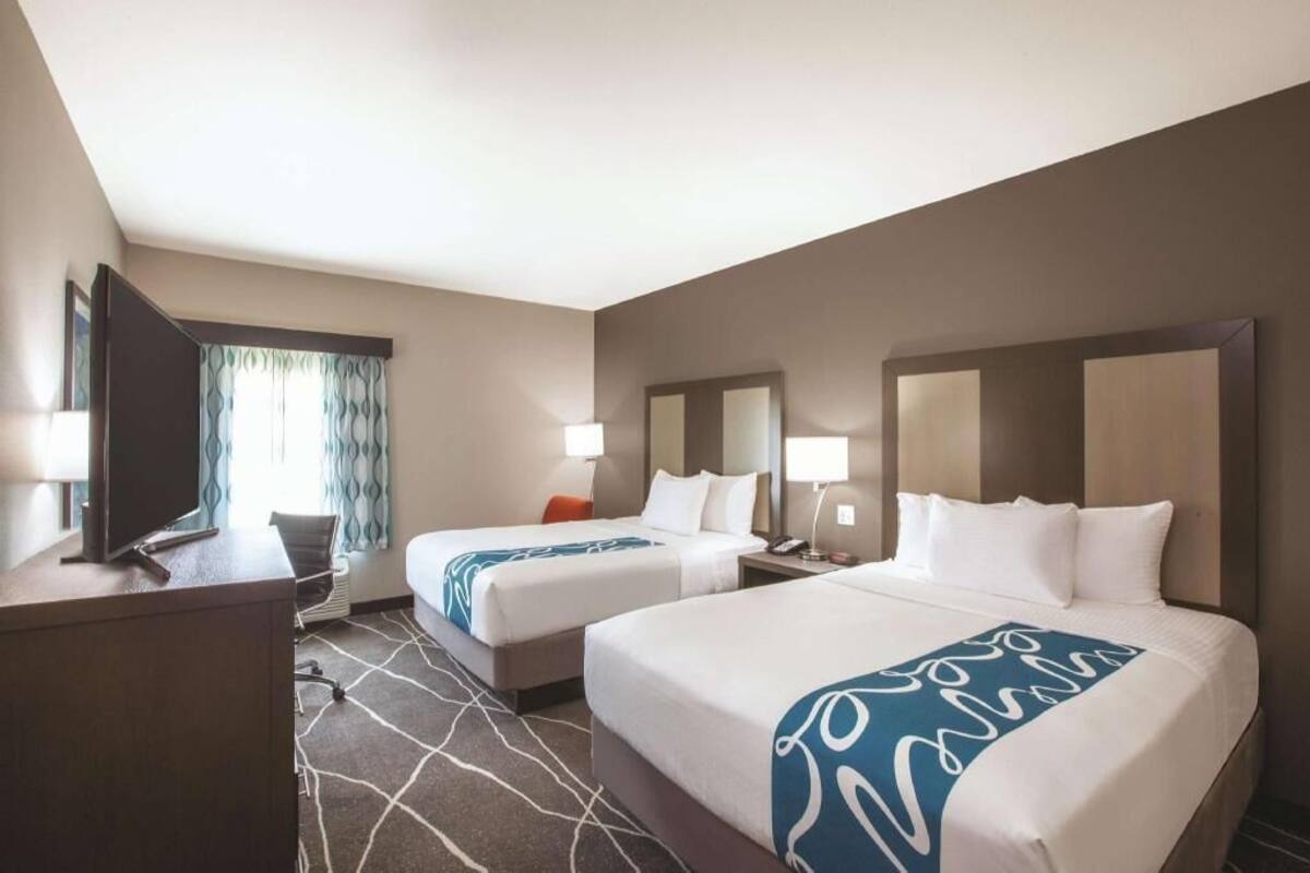 A hotel room with two beds, a desk, a TV, and a window with curtains.