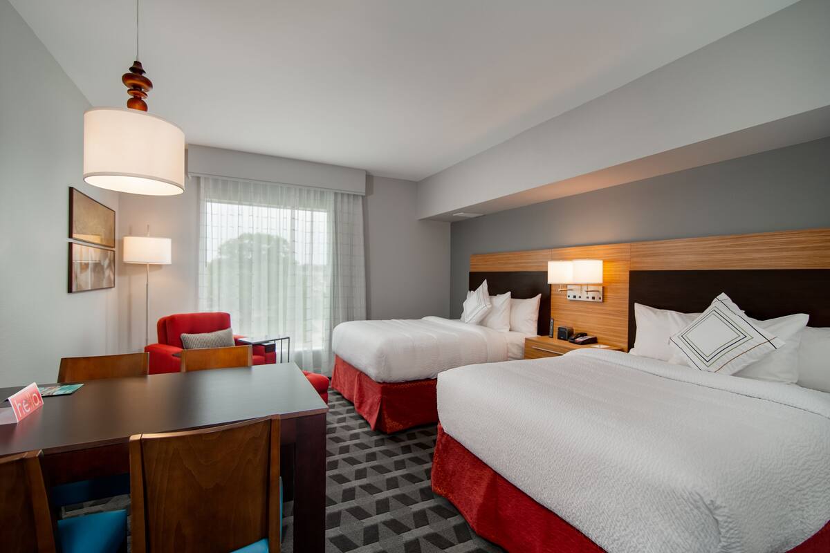 A hotel room with two beds, a desk, a chair, and a large window with curtains.