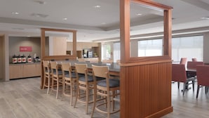 A modern kitchen with wooden cabinets, a central island, and a dining area with wooden chairs and a table. - TownePlace Suites by Marriott Austin Parmer/Tech Ridge (Austin)