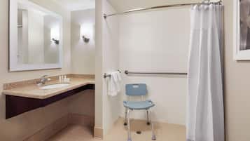 A bathroom with a sink, mirror, shower, and a wheelchair.