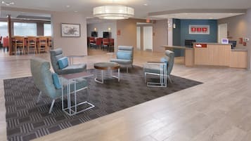 A hotel lobby with seating areas, a reception desk, and a dining area in the background.