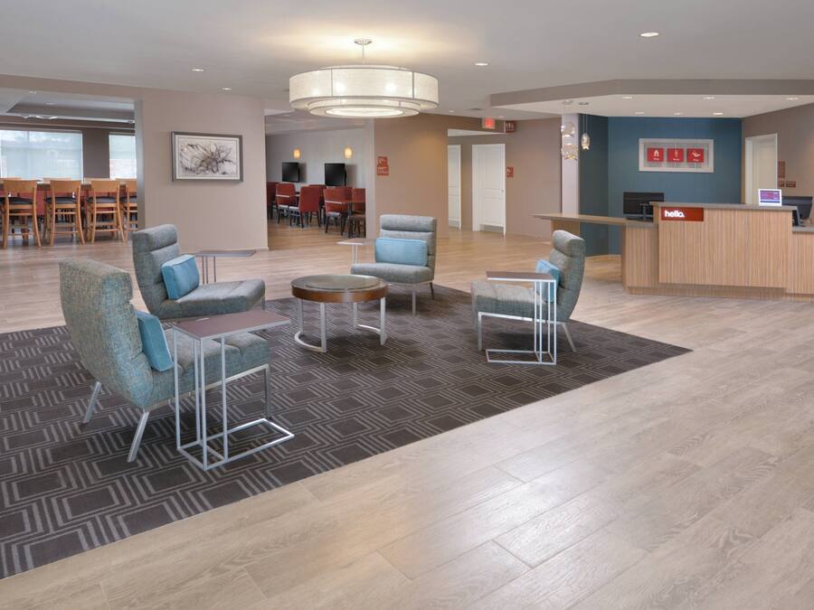 A hotel lobby with seating areas, a reception desk, and a dining area in the background.
