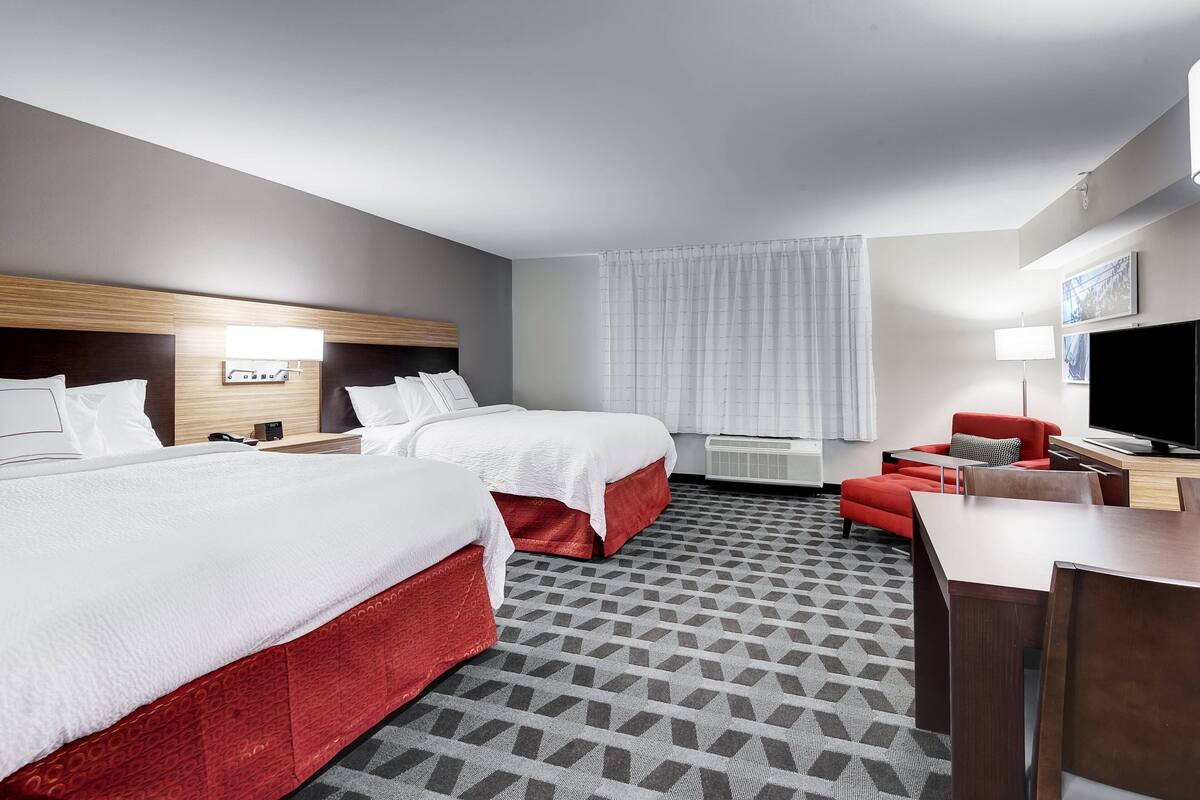 A hotel room with two beds, a red sofa, a TV, and a desk.