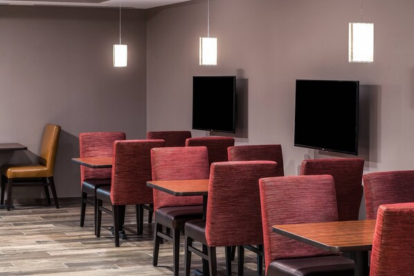 Un espace repas moderne avec des chaises et des tables à revêtement rouge, un téléviseur à écran plat fixé au mur et des luminaires suspendus.