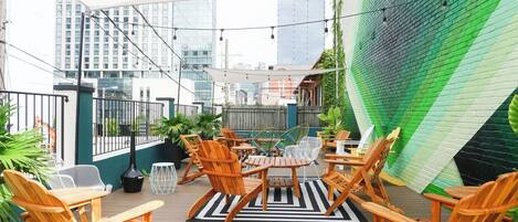 A rooftop patio with wooden furniture, a striped rug, and a view of city buildings.