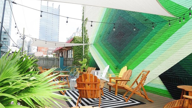 Un área de estar al aire libre con muebles de madera, un tapete de diseño blanco y negro, y un muro de ladrillo verde y negro.