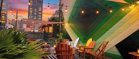 An outdoor seating area with wooden furniture, string lights, and a colorful wall.