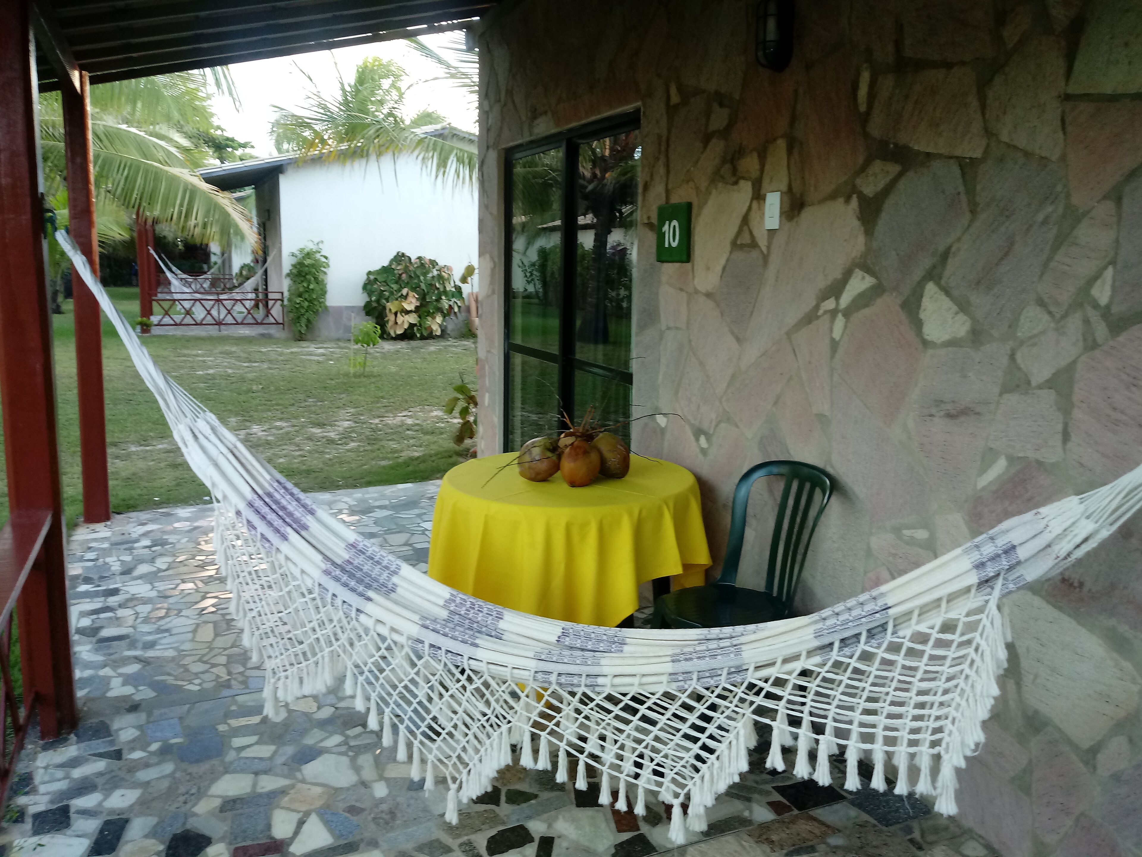 Uma cadeira rede com toalha de mesa amarela, parede de pedra e porta com o número 10.