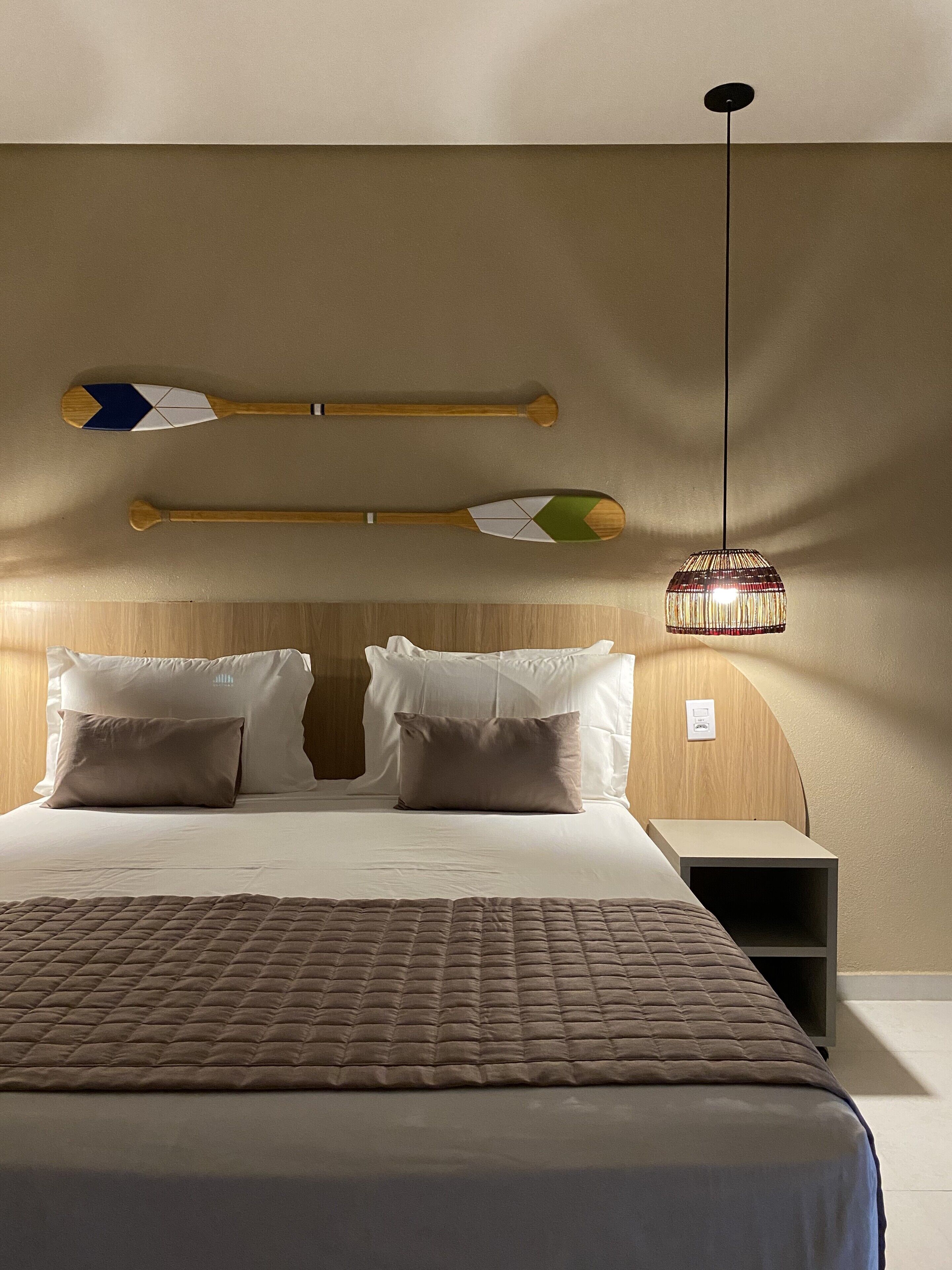 A neatly made bed with a brown quilt, two pillows, and a bedside table with a lamp.