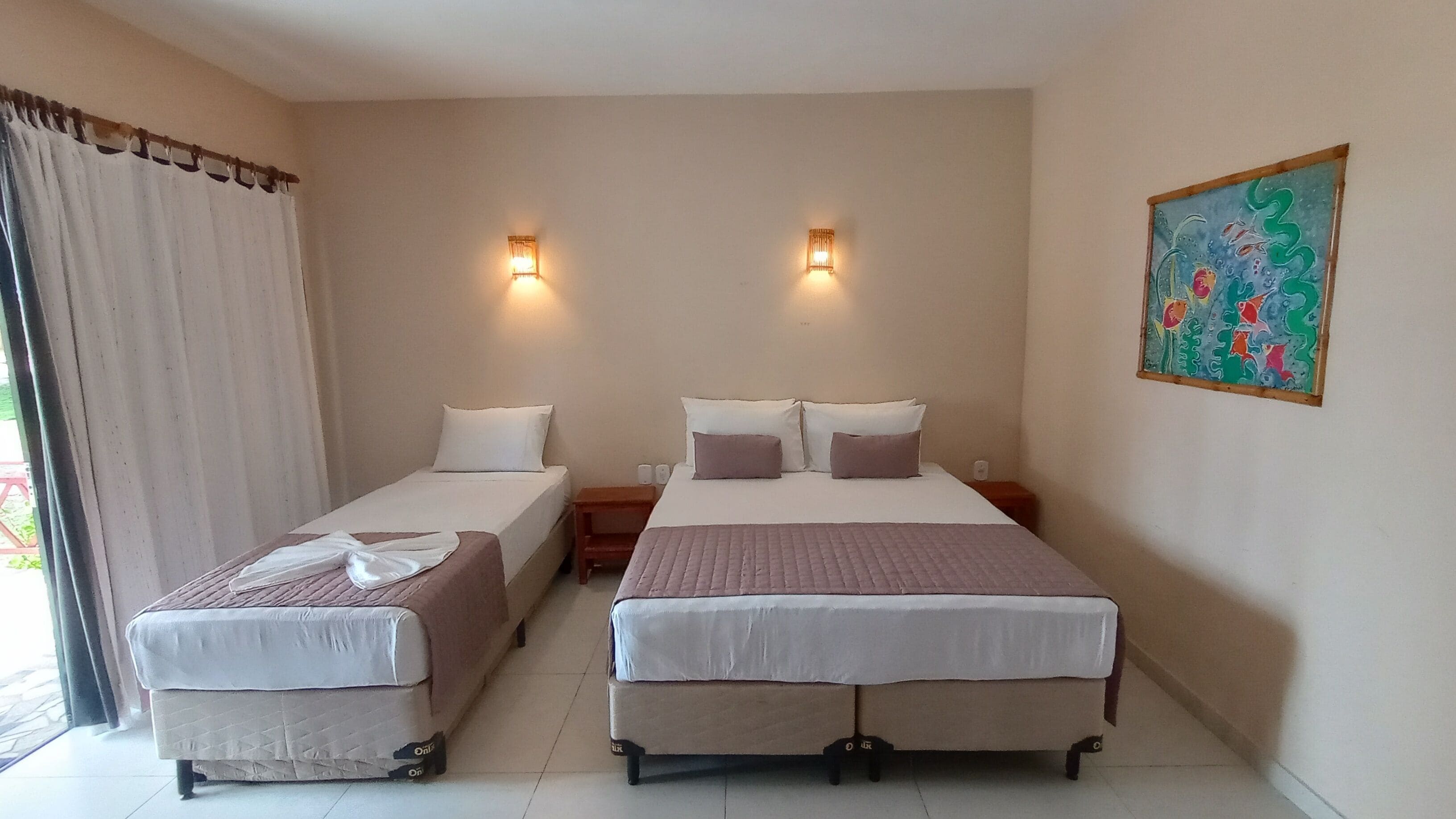 Ein Hotelzimmer mit zwei Einzelbetten, einem großen Fenster mit Vorhängen, einem Bild an der Wand und zwei Wandleuchten.