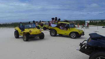 Una playa arenosa con vehículos todoterreno amarillos y gente.