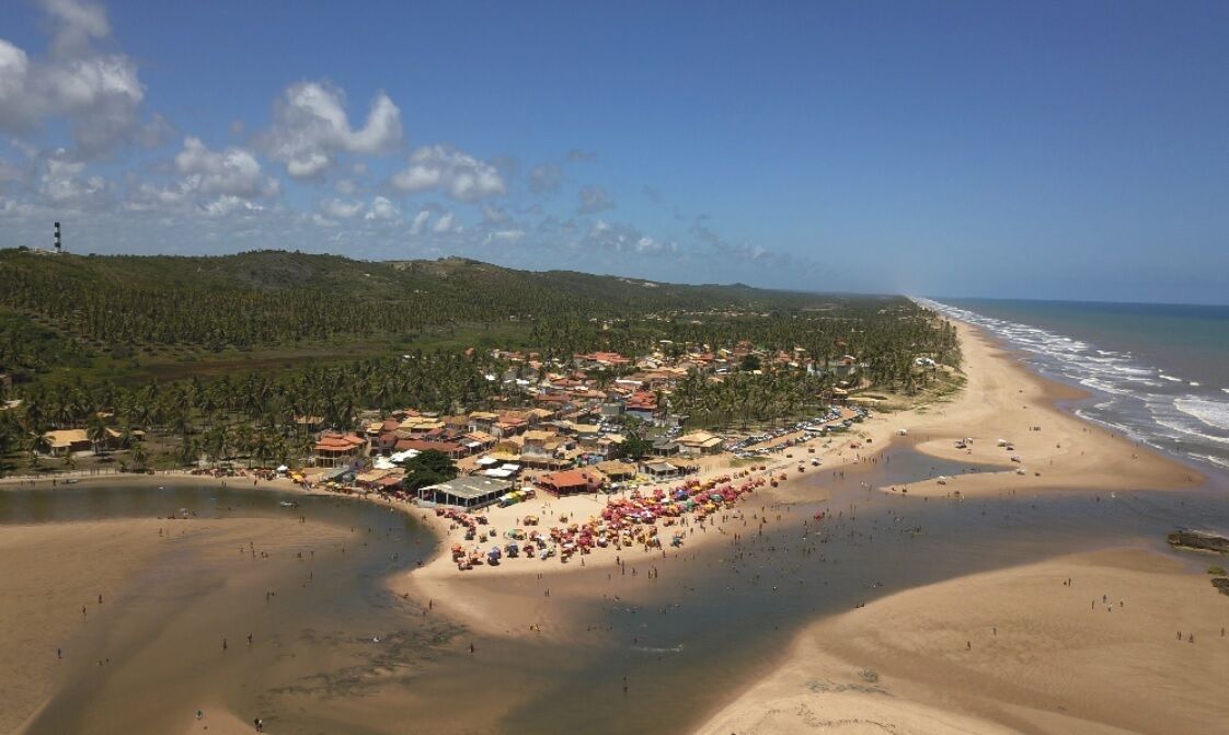An aerial view of a coastal town with a beach, houses, and a lighthouse.