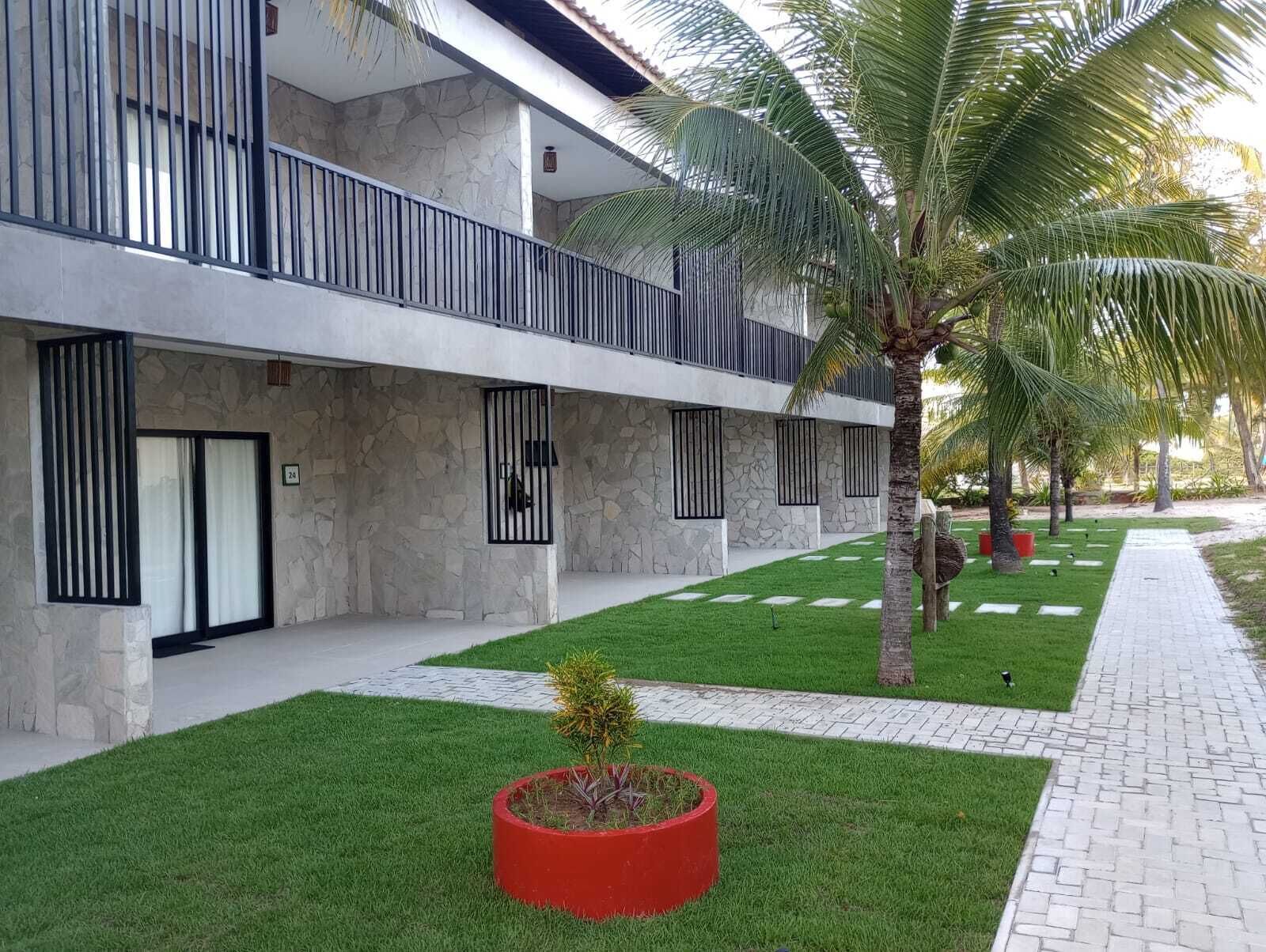 A modern building with a stone facade, multiple balconies, and a well-maintained lawn with a palm tree.