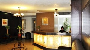 A hotel reception area with a marble counter, a receptionist, and a seating area. - Hotel Marcella Clase Ejecutiva (Morelia)