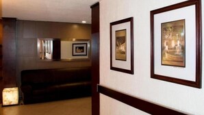 A hallway with framed artwork on the walls, a dark-colored bench, and a light-colored floor. - Hotel Marcella Clase Ejecutiva (Morelia)