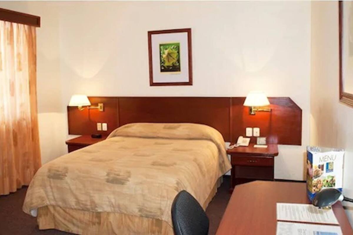 A hotel room with a large bed, two bedside tables with lamps, a framed picture on the wall, and a desk with a computer and a menu.
