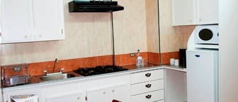 A compact kitchen with white cabinets, a gas stove, a microwave, and a refrigerator.