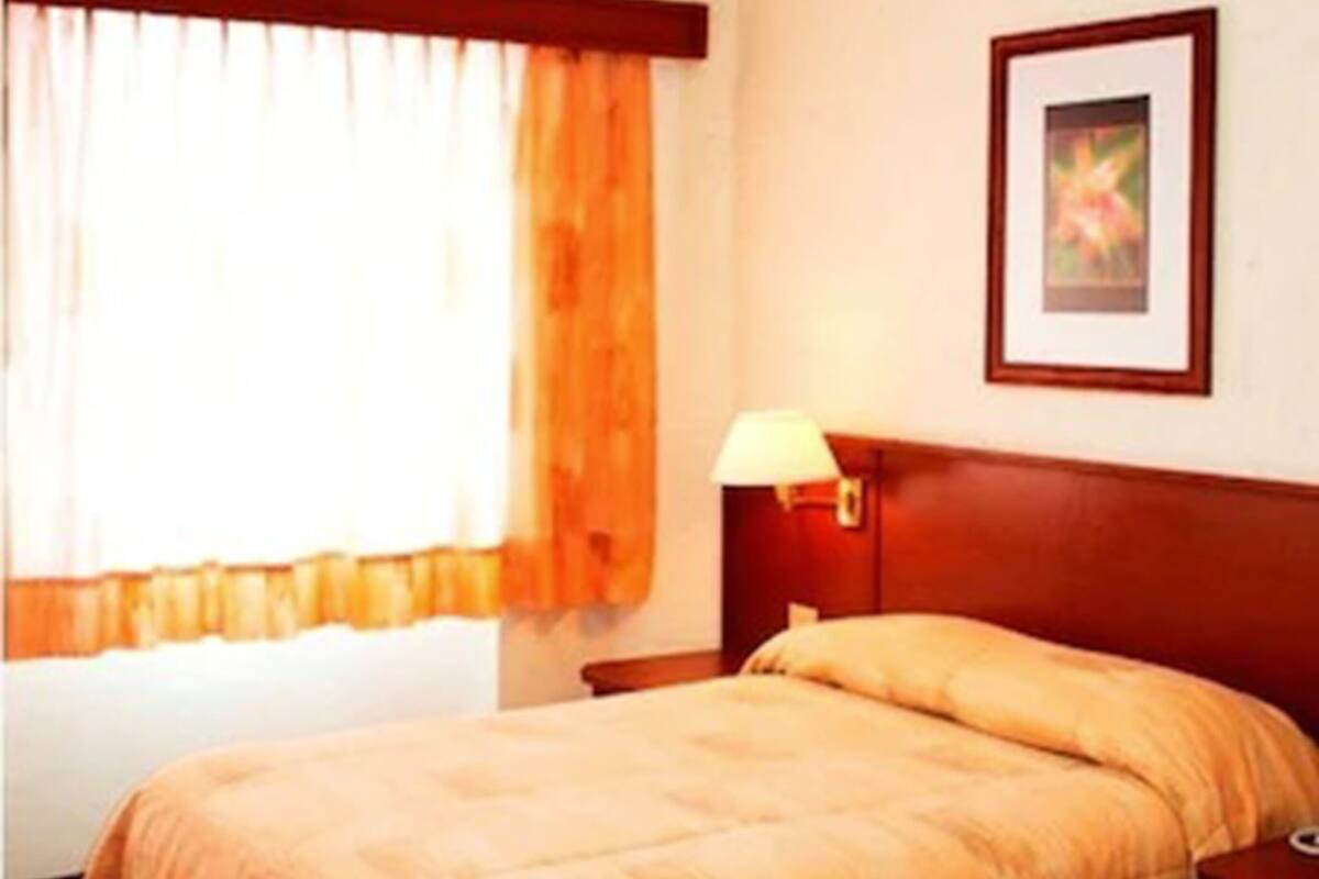 A hotel room with two beds, a window with curtains, a bedside lamp, and a framed picture on the wall.
