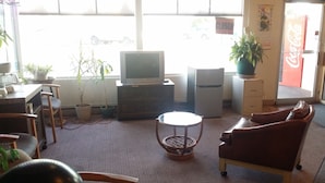 A living room with a television, a refrigerator, a sofa, and a coffee table. There are potted plants and a Coca-Cola refrigerator. - Tahitian Motor Inn (Pasco)