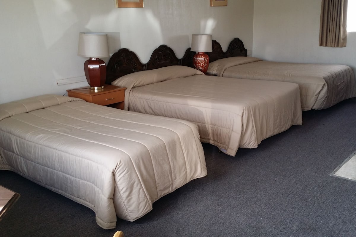 Ein Hotelzimmer mit zwei Einzelbetten, einem Nachttisch aus Holz mit Lampen, einem kleinen Tisch und einem Fenster mit Vorhängen.