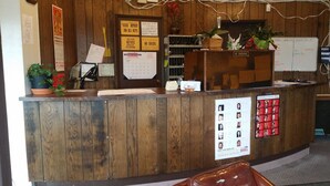 A wooden reception desk with a 'No Smoking' sign, a plant, and a 'Missing Persons' poster. - Tahitian Motor Inn (Pasco)