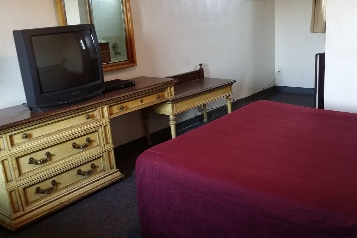 Ein Hotelzimmer mit einem Bett, einer Holzkommode mit Schubladen, einem Fernseher darauf und einem Spiegel an der Wand.