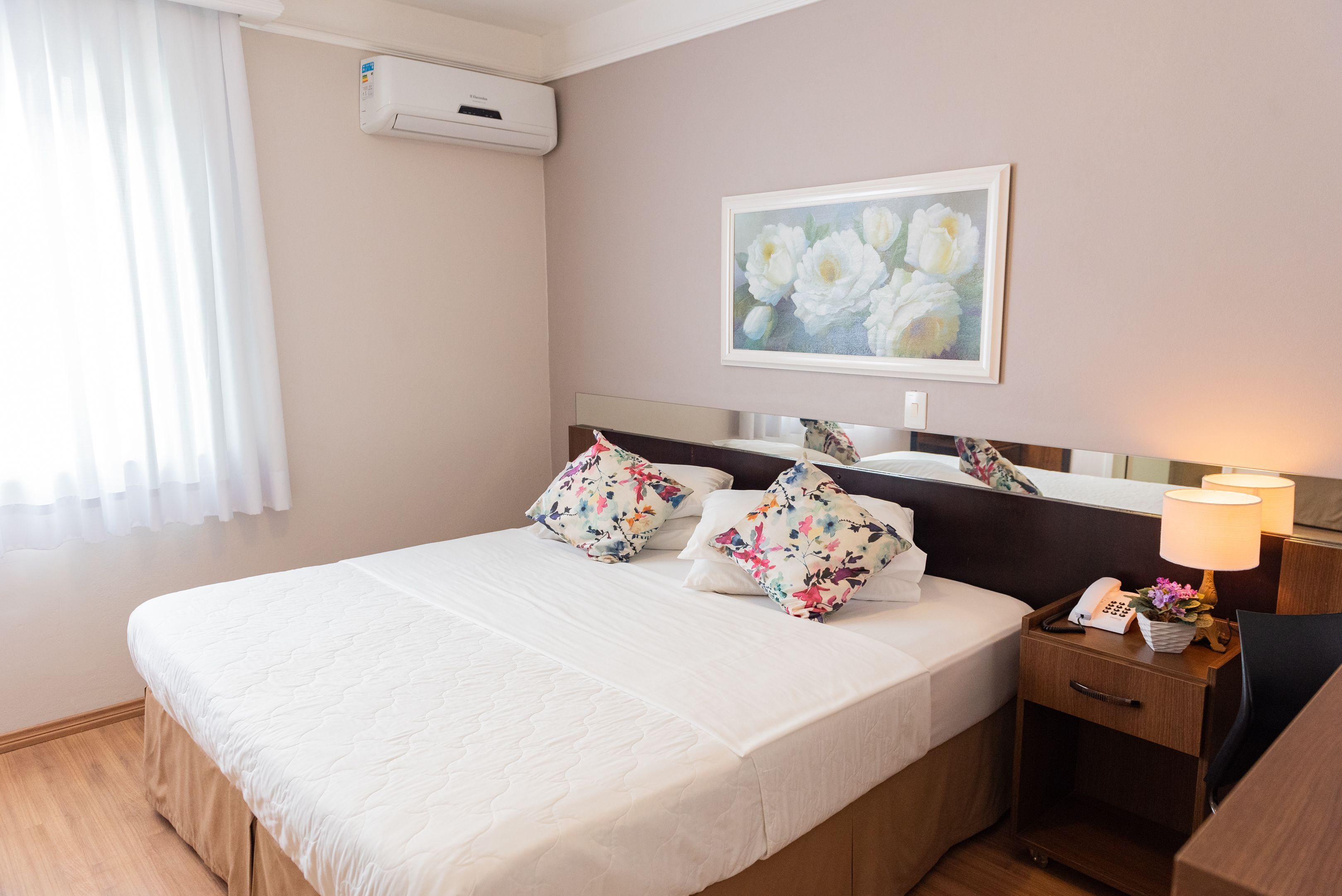 A hotel room with a bed, a nightstand, a lamp, a phone, and a painting on the wall.