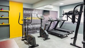 Uma academia com equipamentos de exercícios, incluindo bicicleta ergométrica, elíptico, esteira e máquina de musculação.