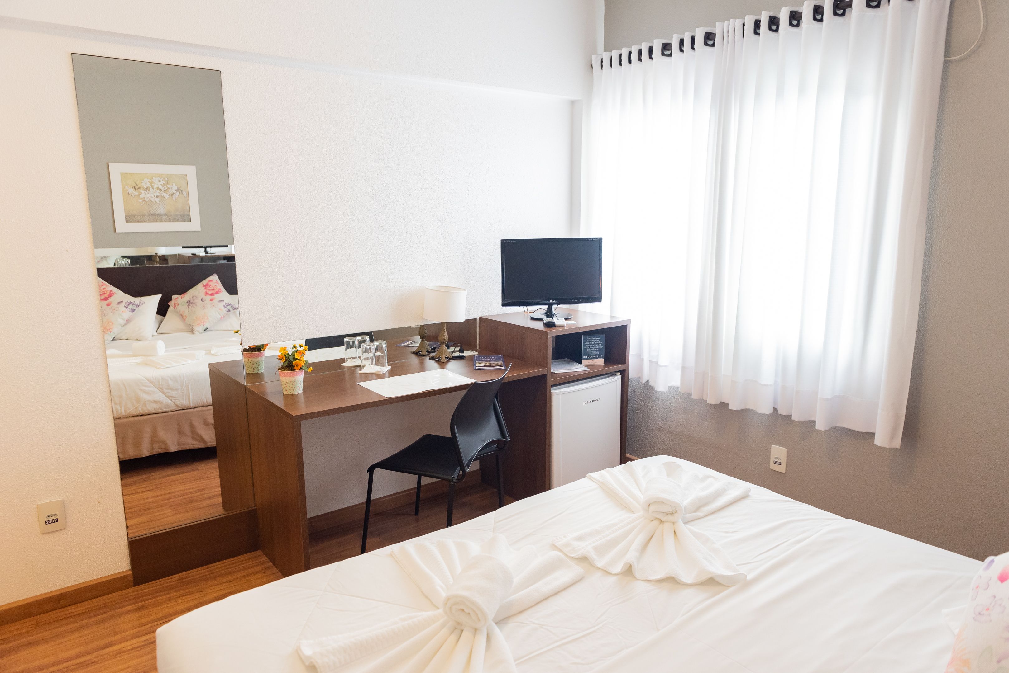 Habitación de hotel con cama, escritorio con computadora, silla y refrigerador pequeño.