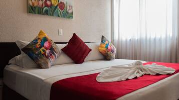 A hotel room with a bed, pillows, a red blanket, and a painting of tulips on the wall.