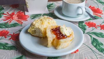 A plate with a scone and jam, a cup of coffee, and a potted plant on a tablecloth with floral patterns.