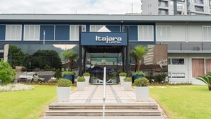 Entrada do Hotel Itajara com design moderno, apresentando fachada de vidro e escadaria que leva à entrada.