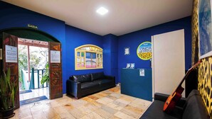 Ein Empfangsbereich mit blauer Wand, einem schwarzen Ledersofa, einer Holztür mit der Aufschrift "SAÍDA" und einer Gitarre, die an der Wand lehnt.