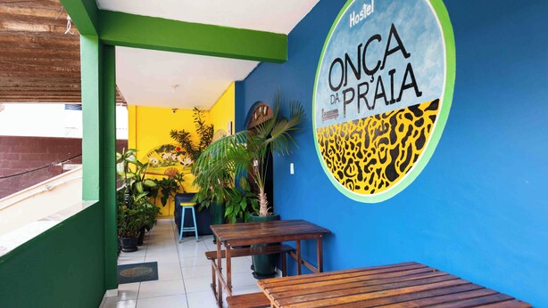 Ein Restaurant mit blauer Wand und Wandgemälde eines Giraffen. Es gibt Holztische und -stühle sowie Blumentöpfe.