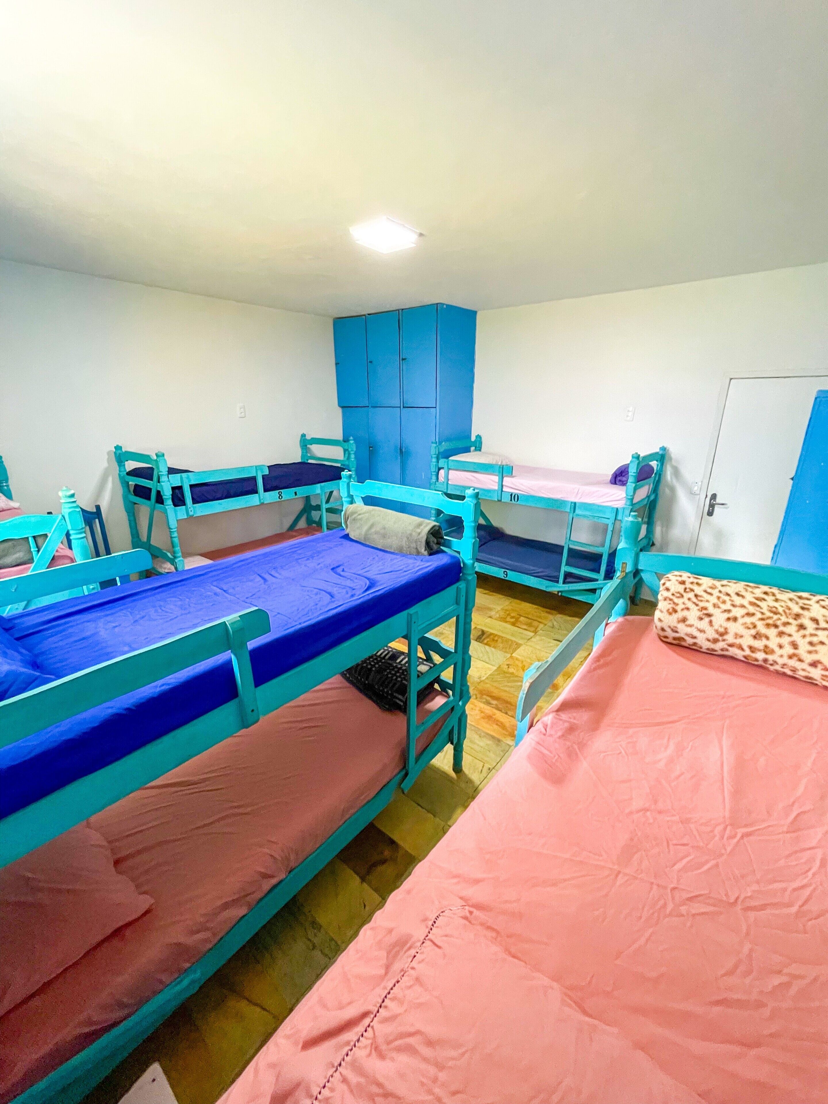 A dormitory room with bunk beds, a wardrobe, and a door.