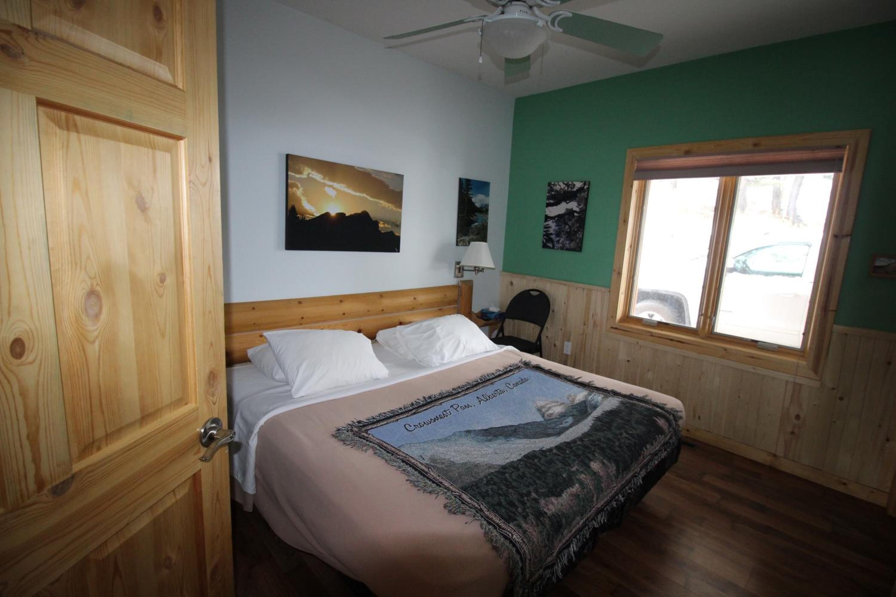 Un dormitorio con cabecera de madera, cama con ropa blanca, ventilador de techo, ventana con persianas y una obra de arte en la pared.