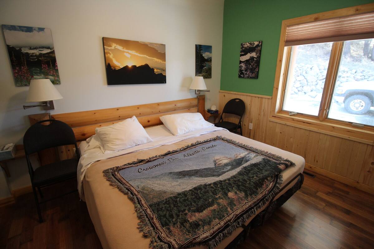 Une chambre à coucher avec un lit, deux chaises, une fenêtre et des œuvres d’art murales.
