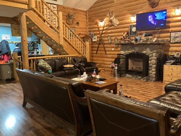 A log cabin interior with a stone fireplace, leather furniture, a wooden staircase, and mounted animal heads. - York Creek Bed and Breakfast (Coleman)